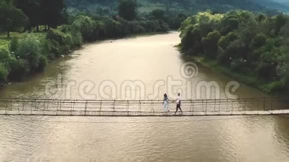 年轻夫妇牵着手女人牵着男朋友在空木桥上走向日落视频的预览图