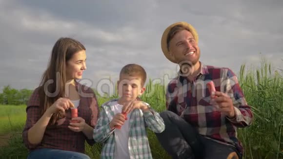 幸福的家庭小男孩和爸爸妈妈一起在野外与天空嬉戏时吹肥皂泡视频的预览图