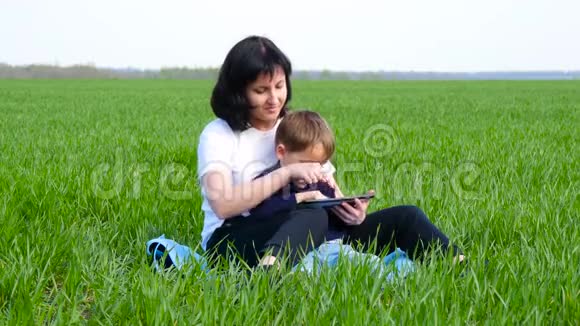 幸福家庭母子坐在绿草上一个母亲和一个小男孩用平板电脑放松技术视频的预览图
