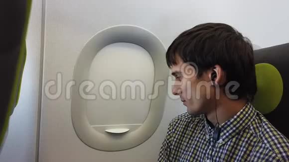 年轻人在飞机上旅行时用耳机听音乐看窗户视频的预览图