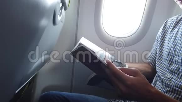 男乘客正在现代飞机上读杂志一个人坐在窗边享受着他的旅行视频的预览图