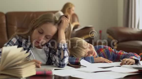 小男孩和小女孩在家学习的前景而他们的母亲坐在背景兄弟倒下了视频的预览图