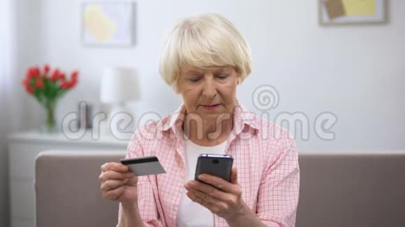 积极的老年妇女在智能手机上输入信用卡号码在网上购物视频的预览图