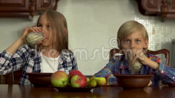 可爱的男孩和女孩从眼镜里喝牛奶小兄弟在厨房的餐桌旁享用健康的饮料视频的预览图