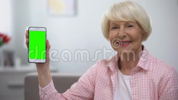 年轻的老妇人在相机上显示带有绿色屏幕的智能手机视频的预览图