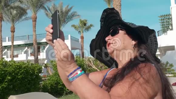 戴着黑帽子的白人老年女性在智能手机上自拍坐在阳光下晒太阳视频的预览图
