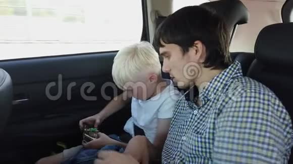 父亲和儿子坐在汽车座椅上玩智能手机而坐在后座上开车视频的预览图