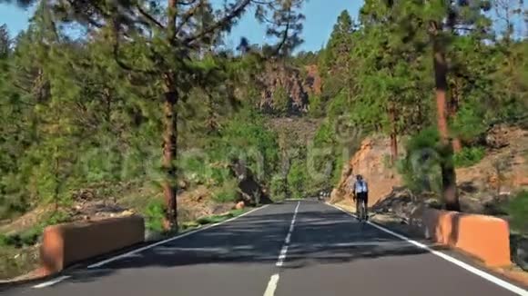 一群未被认出的骑自行车的人在山路上移动周围是岩石景观和针叶树视频的预览图