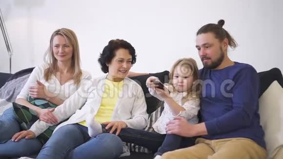 整个幸福的家庭都坐在沙发上通过选择和看电视来放松视频的预览图