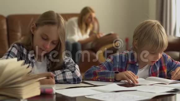 可爱的小男孩和小女孩在家里学习的前景而他们的母亲坐在背景小学生视频的预览图