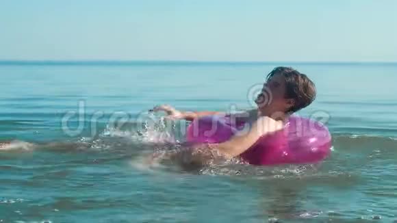 在海里游泳的年轻人漂浮在粉红色的充气圆圈上视频的预览图