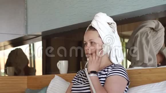 一个头上戴毛巾的女孩坐在酒店的床上在电话里交谈视频的预览图