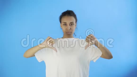 穿着白色T恤的漂亮少女拇指朝下双手放在蓝色背景上视频的预览图