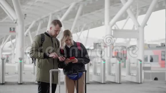 两名乘客正在使用智能手机站在火车站站台上视频的预览图