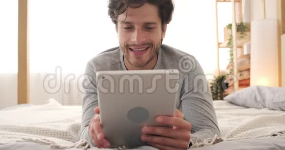 快乐的男人在床上使用数码平板电脑视频的预览图