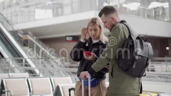 年轻的一对站在机场大厅的智能手机上查看信息视频的预览图