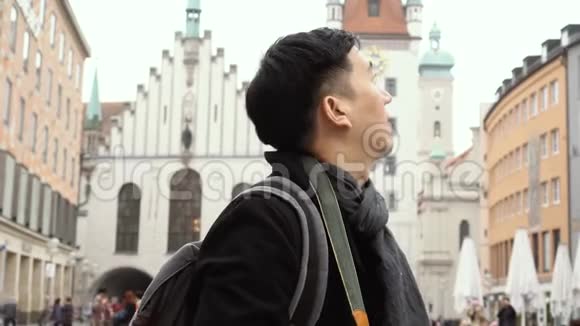 年轻的亚洲旅行背包客在欧洲市中心男子在德国慕尼黑的Marienplatz广场拍照视频的预览图