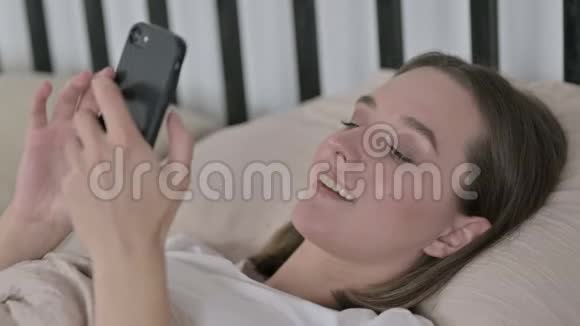 在床上使用智能手机的快乐年轻女子视频的预览图