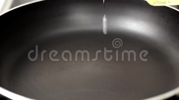 用手将橄榄油倒入一个黑色的热锅中液体在黑暗的表面上扩散视频的预览图