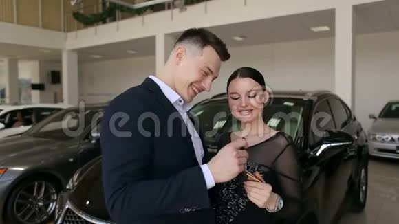 微笑的夫妇拥抱和持有他们的新钥匙在新的汽车陈列室视频的预览图