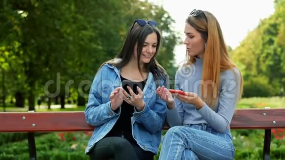 两个女朋友坐在公园的长凳上用手机选择照片视频的预览图