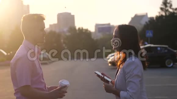 日落时分一对商务情侣在街上边喝咖啡边聊天用手机慢动作视频的预览图