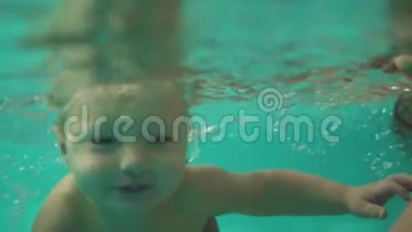 可爱的金发幼儿正在游泳池的水下游泳直到他的母亲帮助他出去一个视频的预览图