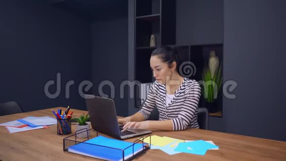 漂亮的年轻女孩在笔记本电脑上工作坐在办公室办公桌室内视频的预览图