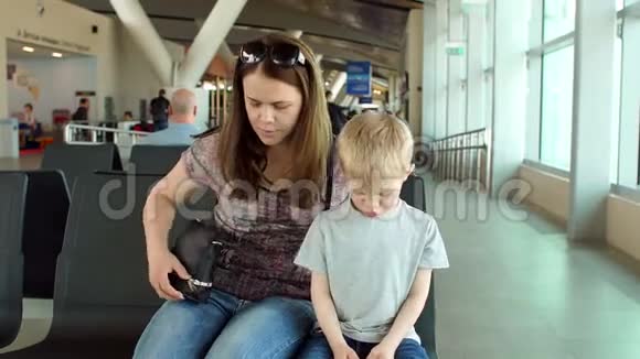 母亲带着一个孩子坐在候机室的长椅上拿着电话视频的预览图