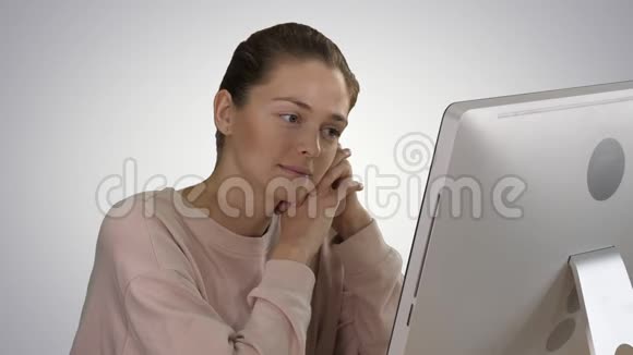 一个穿粉红色套头衫的金发女孩看着电脑显示器在渐变背景下观看视频视频的预览图