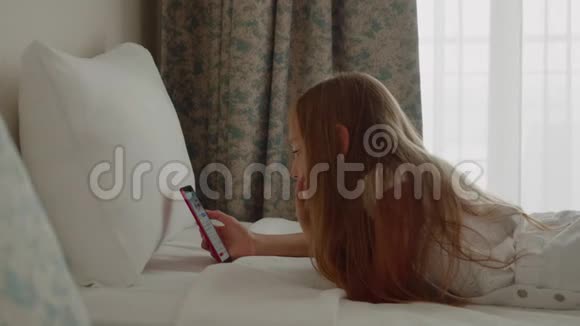 可爱的少女长发躺在床上使用智能手机视频的预览图
