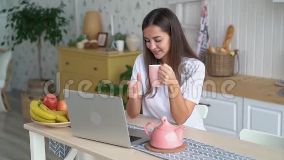 女孩喝咖啡在笔记本电脑上看电影在家享受早晨慢动作视频的预览图