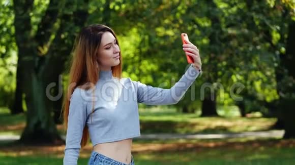 美丽快乐的红发女人在城市公园的手机上自拍视频的预览图