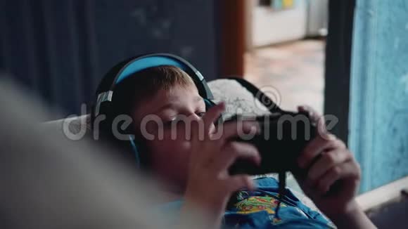 这个男孩在沙发上玩电子游戏头上戴着耳机特写足够了多媒体娱乐视频的预览图