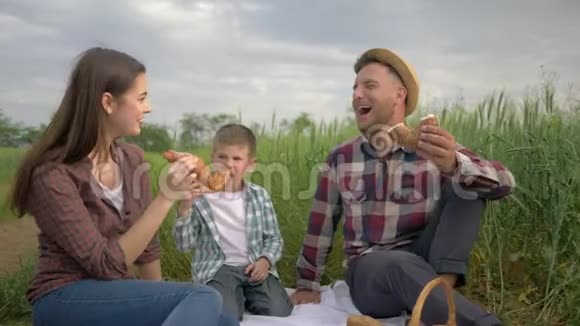 快乐的家庭周末快乐的男人一边给女人喂面包一边和孩子一起在绿色的田野里喝牛奶放松野餐视频的预览图