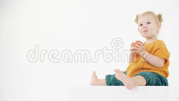 穿着橙色和绿色衣服的宝宝在白色背景下吃苹果视频的预览图