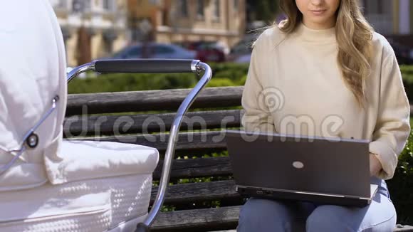 忙碌的妈妈自由职业者在公园的笔记本电脑上工作紧张地摇摆婴儿车视频的预览图