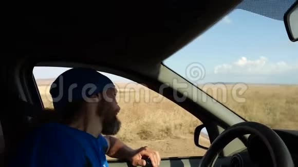 快乐的留着胡子的人在乡村风景中开车司机用手探出侧窗视频的预览图