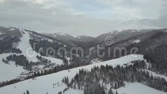飞越喀尔巴阡山脉的一个村庄和它旁边的一个滑雪胜地鸟瞰白雪覆盖的房屋视频的预览图