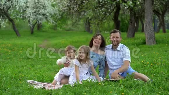 快乐的父母和女儿在春季公园的格子呢上谈笑风生视频的预览图