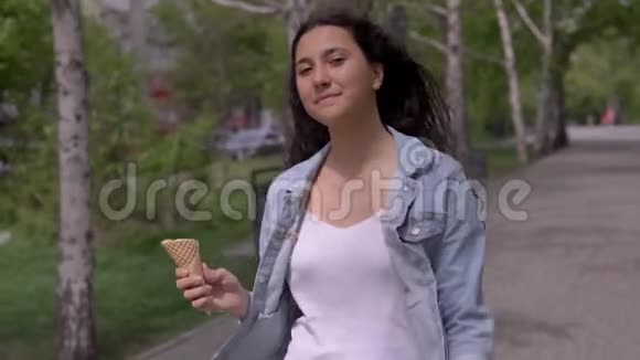 一个漂亮的年轻女孩走在街上在炎热的夏天吃冰淇淋同时心情很好视频的预览图