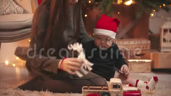 圣诞节概念一个年轻的女人在圣诞工作室和她的小宝宝玩一个抱着玩具鹿的婴儿视频的预览图