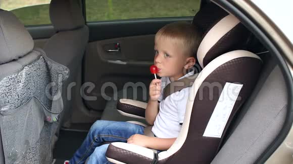 一个可爱的小男孩坐在车里的汽车座椅上吃一根棒棒糖慢动作视频的预览图