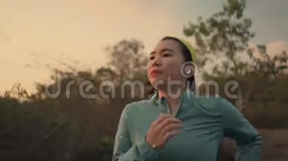 年轻健康的亚裔韩国妇女日落时分在树林里跑步进行慢跑锻炼时的跟踪万向节镜头视频的预览图