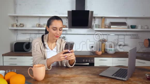 家庭主妇坐在厨房里检查社交网络视频的预览图
