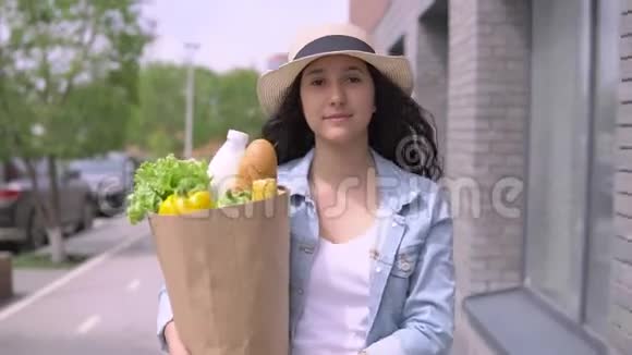 年轻漂亮的女人穿着牛仔夹克和帽子带着一个包装产品有一个好心情和微笑4K视频的预览图