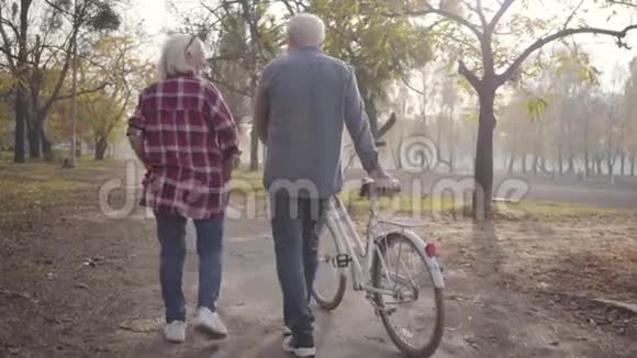 成熟的白人夫妇骑着自行车在公园的小巷里散步快乐的退休老人家庭秋天视频的预览图