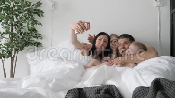 开朗的年轻家庭在躺在床上用手机做有趣的自拍视频的预览图