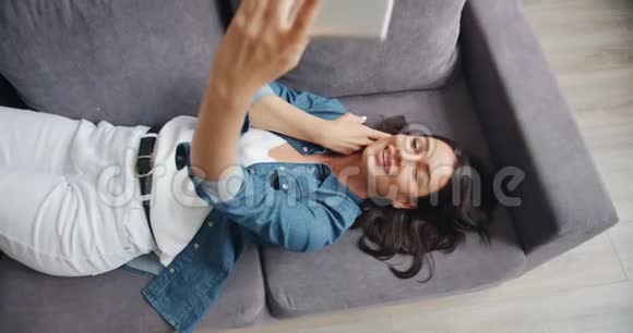 慢动作性感的年轻女人在沙发上用智能手机自拍视频的预览图