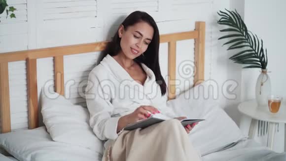 穿着白色浴袍的年轻美女躺在床上看书视频的预览图